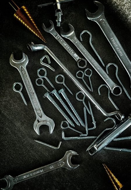 A collection of metal wrenches, screws, and drill bits arranged artistically on a dark background.
